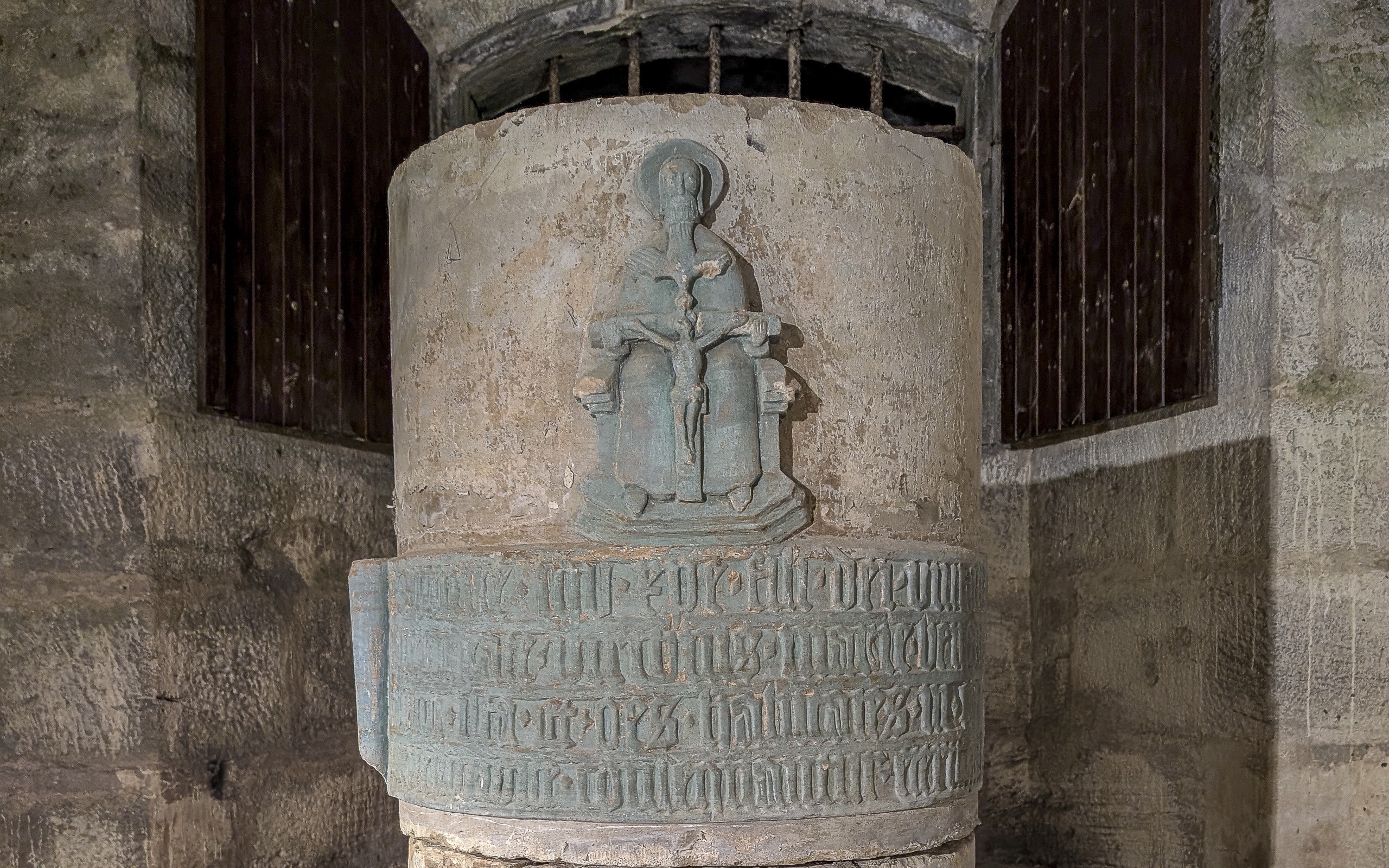 Steinsäule im gewölbten Durchgang der Bastion, oben ein grünlich gefasstes Relief der Dreifaltigkeit, darunter eine Schriftkartusche in gotischen Minuskeln