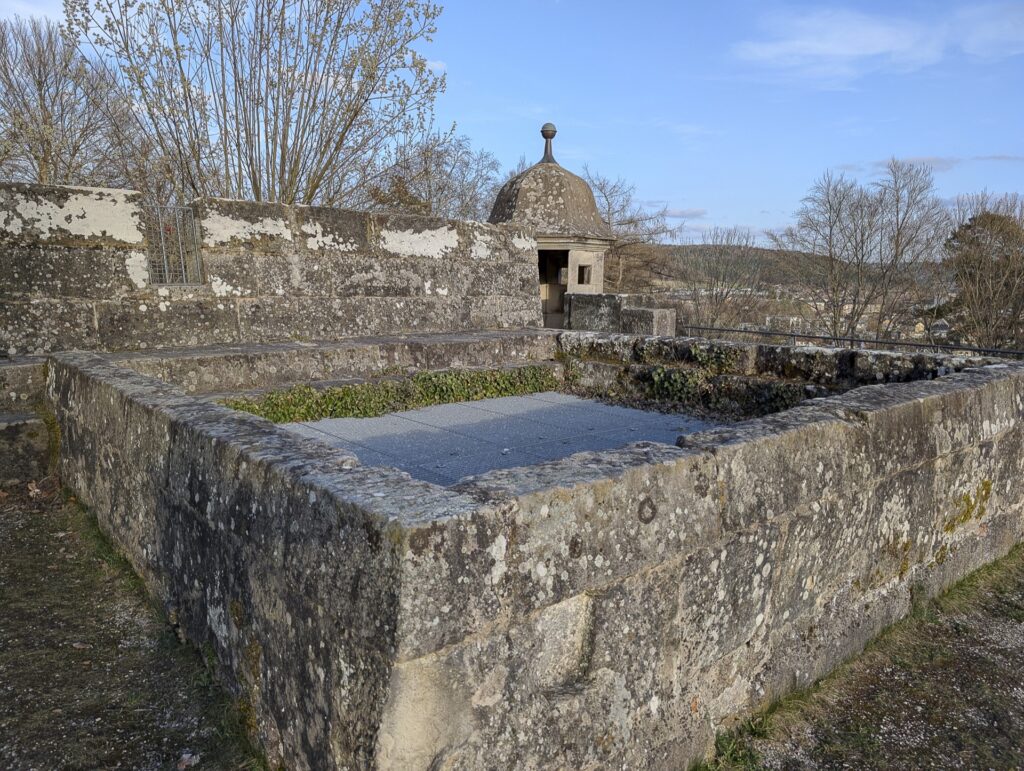 Gemauerte, vergitterte Brunnenöffnung im Kugelgarten der Festung, im Hintergrund ein Wachhäuschen